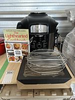 Ninja Foodi Deluxe Cooker in black with included cookbook and dehydrator rack on top of its original box.