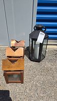Four lanterns arranged outdoors: one large black metal lantern with battery-operated candle, and three smaller wooden lanterns with copper tops for tea lights.
