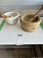 Two mortar and pestle sets on white surface, white stone small set and beige ceramic larger set with wooden pestles.