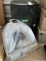 Portable AC unit in black with LG logo alongside wrapped connecting hose and window kit panels.