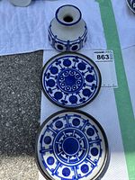 Small vase and two matching plates with vibrant blue pattern arranged on white paper towel outdoors. Vase has geometric blue design and plates have circular blue patterns.