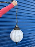 Retro hanging lamp suspended by a chain shown against a blue backdrop, hand holding the chain for scale