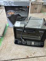 Black Cuisinart convection toaster oven with control panel below the glass door, topped with a chrome rack. Kuraidori induction cooktop box behind.
