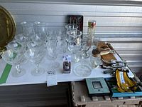 Photo showing assortment of wine glasses, tall etched dated glasses, small crystal sherry glasses, and bar tools on a table.