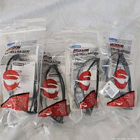 Four sealed packages, each containing one pair of Jackson V40 HellRaiser safety glasses, showing the sealed bags and red safety glasses icon on packaging.