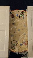 Top view of the large ceramic Christmas platter bowl inside protective packaging, showing snowman and penguin holiday designs with snowflakes and red scalloped edges.