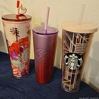 Three Starbucks branded tumblers with lids and straws displayed side by side, showing distinct designs and colors.