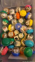 Top view of multiple vintage NFL mini ceramic mugs inside plastic capsules with colorful lids in a storage bin.