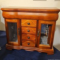 Front view showing wooden jewelry case with glass panel doors and four drawers in the center.