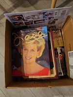 Box containing multiple Princess Diana books with a cover showing a close-up portrait photo of Princess Diana, some paperback and hardcover books visible.
