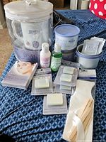Complete view of Satin Smooth wax warmer, multiple wax containers, individual wax bars, applicator sticks and pre/post waxing solution bottle on blue cloth surface