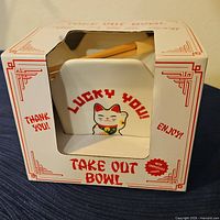 Front and side view of the boxed ceramic take out bowl featuring a Lucky You cat design, with chopsticks included inside the box.