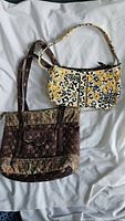 Two Vera Bradley cloth bags shown on white background, a yellow floral shoulder purse and a brown paisley larger tote