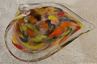 Top view of the leaf-shaped handblown glass candy dish showing colorful swirls of orange, yellow, red, blue, and purple within clear glass.