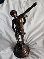 Full view of bronze sculpture showing figure with outstretched arm and circular base.