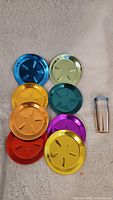 Photo of eight colorful aluminum coasters arranged in two columns, and one shiny aluminum shot glass beside them.