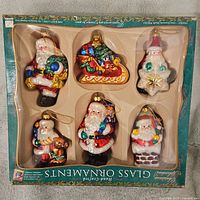 Full view of all six glass Christmas ornaments in the original packaging box labeled Splendeur, showing detailed Santa Claus and sleigh designs.