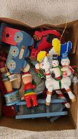 Box filled with various vintage wooden Christmas ornaments including a blue red train, two snowmen on a white horse, and other colorful wooden figures.