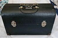 Front view of a black vintage hard case with metal locks and corner protectors.