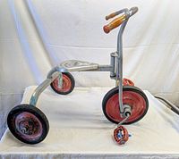 Side view of vintage 1950s Angeles cast aluminum tricycle showing frame, tires, seat, and handlebars.