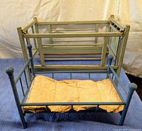 Two wooden doll cradles placed on blue and white fabric, showing overall shape, paint condition, and mattress included in the blue cradle.