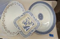 Three ceramic serving pieces: large oval platter with blue floral border, square bird dish with blue bird and floral design, and another oval platter with intricate blue patterned border.