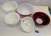 Five mixing bowls arranged on a white surface, showing two large bowls and three smaller bowls including milk glass and Pyrex.