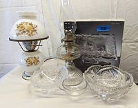 Lot showing all six items: crystal cake pedestal in box, glass basket, cut glass bowl, canning funnel, and two hurricane lamps.
