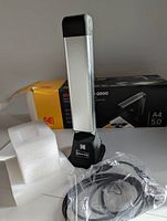 Kodak Nuscan Q500 scanner standing upright in front of its damaged original box, with foam protective packaging and USB cable visible.