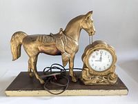 Front view of the gold-painted metal horse and clock on wood base.