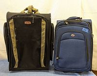 Two travel suitcases side by side, Route 66 on left in black with beige stripes, American Tourister on right in blue fabric with front zipper pocket