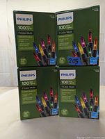 Four sealed boxes of Philips 100 count mini Christmas lights, multi-color, arranged upright to show front and side of packaging prominently displaying product details.