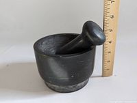 Photo showing the mortar with pestle inside next to a ruler for size reference.