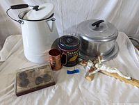 Wide view of all lot items showing enamel pitcher, tobacco tin, cake tote, pipe bowls, and figurine