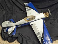 Side angled view of RC model airplane showing color pattern of blue, black and white with clear canopy and visible two-blade propeller with wooden nose framework