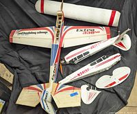 Top view showing large Extra 330SC wing, fuselage with propeller, and Delta Darter fuselage and tail parts in red and white colors.