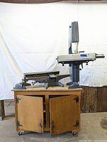 Front view of Shopsmith bandsaw mounted on wooden cabinet with two doors opened, showing size and base structure