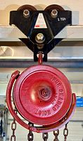 Close-up of the red spur geared hoist with chain and hook attached to the black steel beam trolley marked '1 TON'.