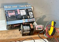 Champion 2000 lb electric winch on wooden board with hooks, original box behind