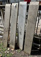 Four aluminum motorcycle ramps standing vertically showing diamond plate pattern.