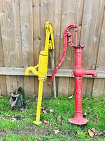 Three antique cast iron water pumps lined up outdoors by a wooden fence: one red, one yellow, and one smaller green pump.