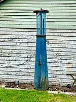 Front view entire gas pump against white siding showing fluted glass reservoir and conical base