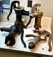 Four antique hand water pumps shown on countertop, highlighting varied conditions and metal finishes.