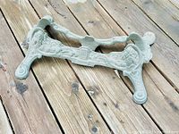 Overall view of the cast iron bicycle stand placed on wooden deck, showing its full shape and ornate Victorian decorative style.