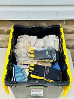 Bin filled with multiple pairs of work gloves of different types including leather and fabric gloves, some sealed in plastic packaging.