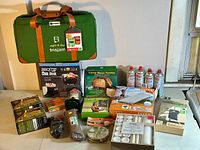 Camping gear assortment including Frisjam game bag, Coleman butane canisters, BBQ grill accessories, camp stove toaster, camping lantern, camping rope, and boxed camping mat.
