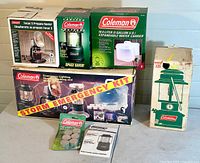Full lot overview with the emergency kit box, propane heater box, space saver lantern box, expandable water carrier box, vintage metal lantern box, tub candles, and manuals, displayed on a surface against a plain background.