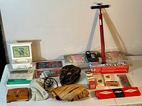 Wide view of lot showing baseball gloves, coin wrapper kit, wooden box, boxed games, fishing lures, and bicycle pump