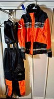 Full view of the Harley Davidson two-piece motorcycle rainwear set hanging on hangers showing orange and black jacket and pants.