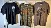 Three Harley Davidson branded t-shirts hanging on hangers showing front designs.